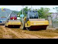 A construction site with a yellow caterpillar grader moving land and a roller working on the road